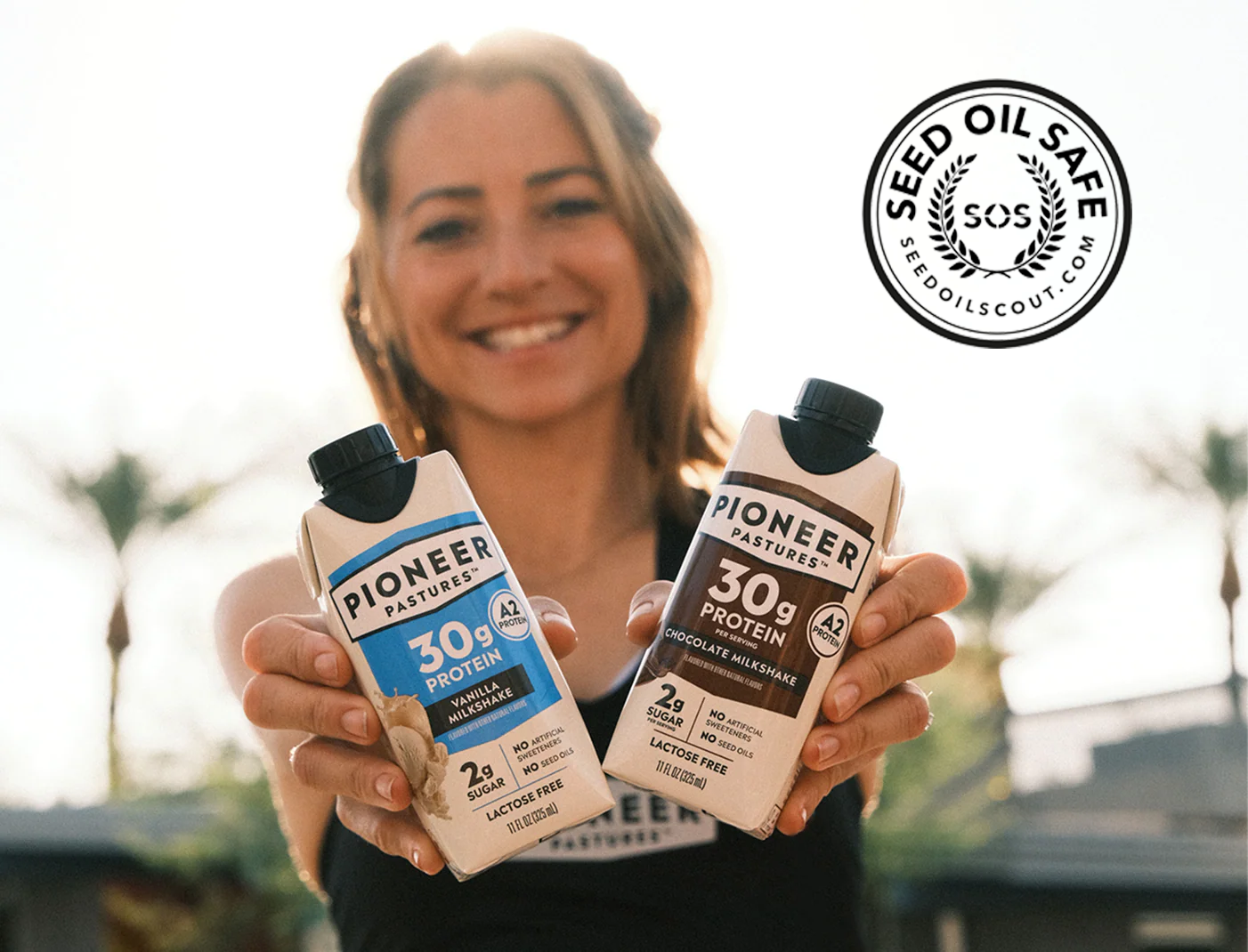 Woman holding two Pioneer Protein products with a 'Seed Oil Safe' logo in the corner.