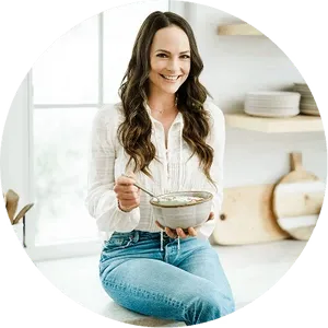 Kelly LeVeque sitting on the floor eating from a bowl in a home setting