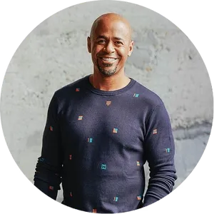 Sean Croxton wearing a navy sweater with colorful patterns against a textured wall.