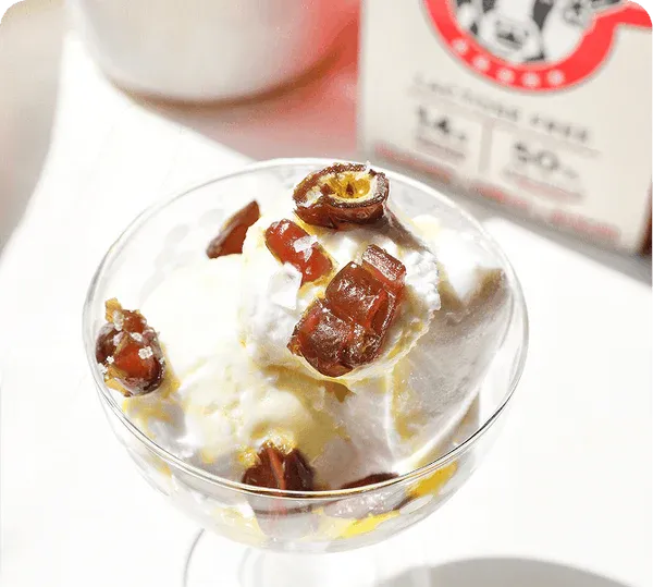 Dessert with yogurt and dried fruits in a glass bowl on a white surface.