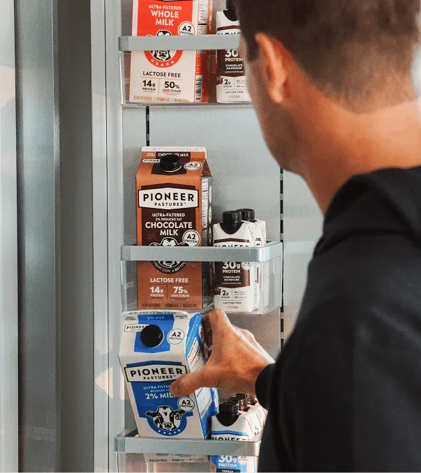 Person reaching for a carton of Pioneer Pastures milk on a refrigerator door.